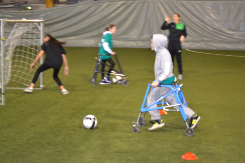 Two participants using walking frames playing football with coaches